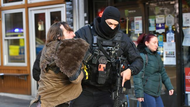 A police officer moves an uninvolved person away from a cordon amid tense scenes.