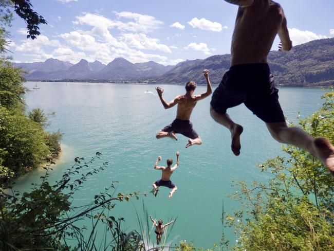 Photo sequence of a young man leaping off a cliff into a blue Alpine lake below on a hot summer day. Slight motion blur on young man as he flies through the air.