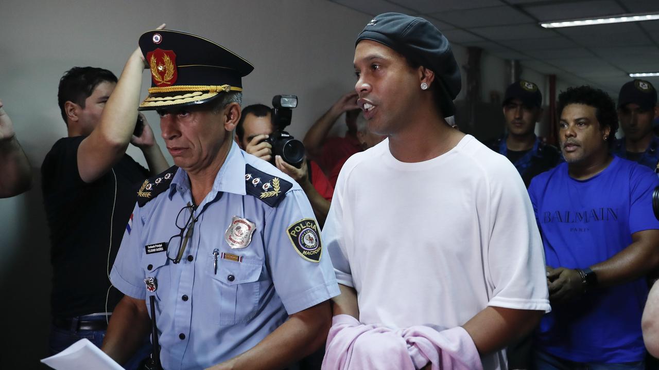 Ronaldinho escorted by police after being arrested for using a fake passport.