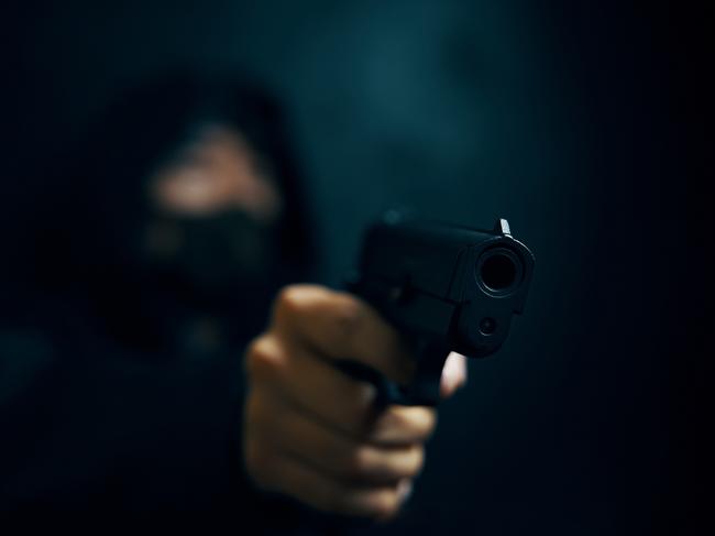 Man in hood threatens with firearm. Masked robber with gun. Weapon in person's hands. Murderer or armed thief. Criminal with pistol. Generic image. Picture: Savusia Konstantin