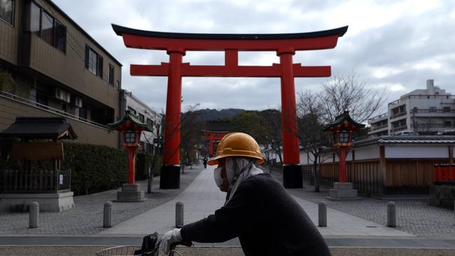 A man wearing a face mask cycles through the Shrine gate outside of the Fushimi Inari-taisha shrine. Picture: Getty