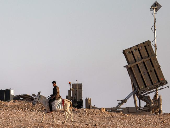 TOPSHOT - A boy rides a donkey near one of the batteries of Israel's Iron Dome missile defence system at a village not recognised by Israeli authorities in the southern Negev desert on April 14, 2024. (Photo by AHMAD GHARABLI / AFP)