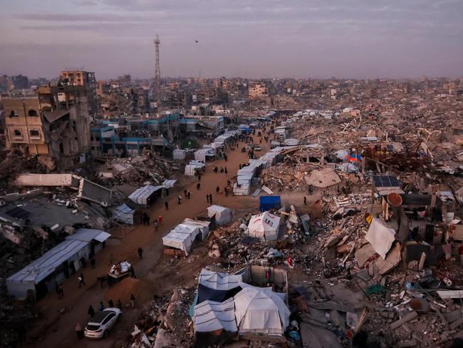 TOPSHOT - Palestinians walk past tents lining the streets amid the rubble of destroyed buildings in Jabalia, in the northern Gaza Strip on February 18, 2025, as people return to northern parts of Gaza during a current ceasefire deal in the war between Israel and Hamas. Israeli Prime Minister Benjamin Netanyahu said on February 17, that he was "committed" to US President Donald Trump's plan for Gaza, which involves displacing more than two million inhabitants of the Palestinian territory. (Photo by Omar AL-QATTAA / AFP)