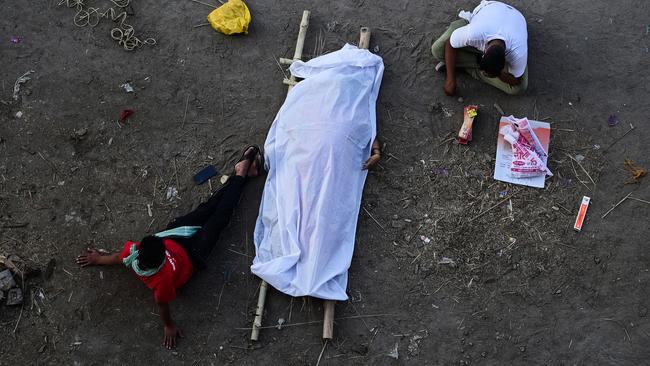 Relatives sit on the banks of the Ganges river, next to the body of a family member who is believed to have died of Covid-19, while waiting for a funeral pyre to become available, in Allahabad, India. Picture: Getty