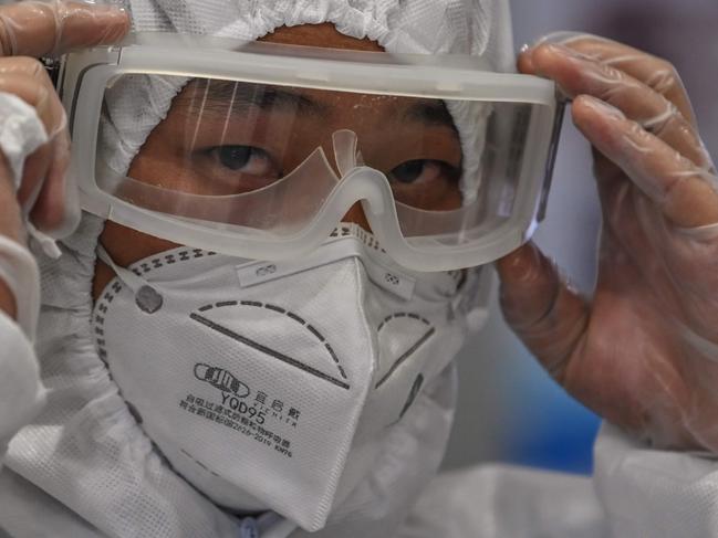 TOPSHOT - A member of the airport security wearing protective gear as a preventive measure against the COVID-19 coronavirus outbreak monitors passengers as they exit following their arrival at Shanghai Pudong International Airport in Shanghai in March 26, 2020. (Photo by Hector RETAMAL / AFP)