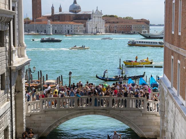 Venice, Italy - 5 September 2017 as usual, the canals and bridges are jam-packed with tourists. Venice is one of the great cities of the world, famed for its canals, sublime architecture, beauty and exotic history. It is also inundated by tourists for much of the year, stupidly expensive, often smelly and slowly sinking into the Adriatic. Oh dear - you pick. The canals of Venice are its life - blood; they are the most important way of getting around for local and tourists alike. Public transport by water busses - vaporetti - and water taxis is quick and efficient. Needless to say, only tourists use the gondolas! Here we see the Ponte della Paglia, a small bridge which links the front of Palazzo Ducale to the front of the new prison. In the distance, we see the Basilica di Santa Maria della Salute.image: getty Imagesescape16 may 2021kendall hill