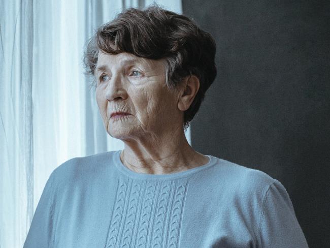 Copy space of blind elderly woman next to window with folded white cane against black background