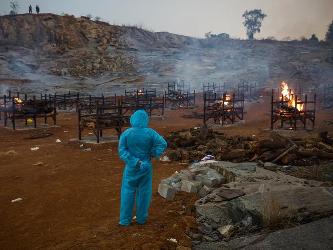 A man wearing PPE (Personal Protective Equipment) watches mass cremations in a disused granite quarry repurposed to cremate the dead due to COVID-19 in Bengaluru, India. Picture: Getty Images