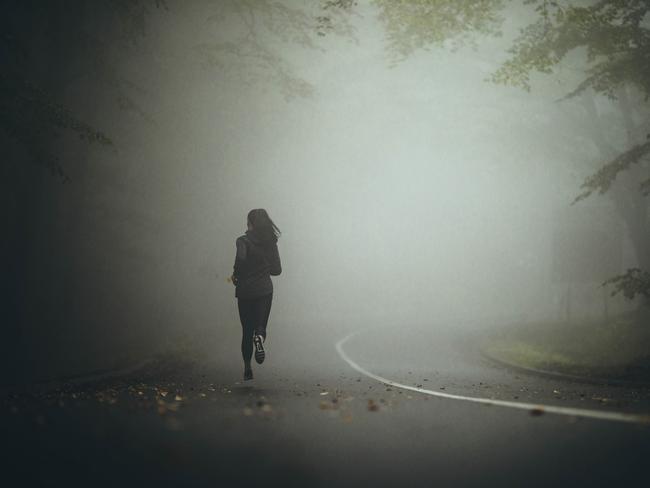 Back view of determined athletic woman jogging during bad weather conditions in forest. Copy space.