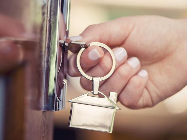 Woman using a house key on the front door. Close up of he woman??s hand. She is turning the key in the lock. There is a hallway in the  background. The key ring has a house icon on it.