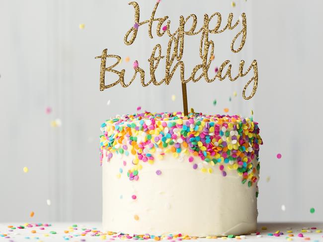 Colorful birthday cake with golden happy birthday banner and falling sprinkles