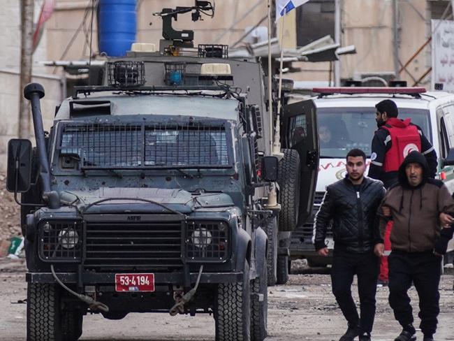 Palestinians walk past an Israeli forces armoured vehicle during a military raid in Jenin, in the occupied West Bank on January 22, 2025. A Palestinian official reported shooting and explosions in the flashpoint West Bank town of Jenin on January 22, as Israeli forces pressed a raid that the military described as a "counterterrorism" operation. (Photo by AFP)