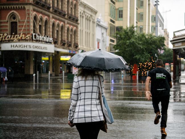 A woman is seen walking with an umbrella as a man runs across at the King William Street and Rundle Mall crossing as Adelaide experiences rainy weather in the first few days of summer, Adelaide, Monday, December 2, 2019. (AAP Image/ Morgan Sette)