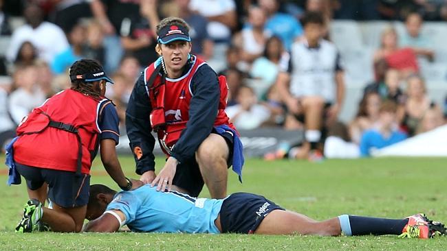 Waratahs centre Kurtley Beale lies prone on the turf and receives some attention from trainers.