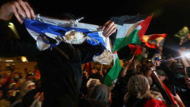 A Palestine supporter holds a burnt Israeli flag into the air during a rally outside the Sydney Opera House on October 9. Picture: Getty Images