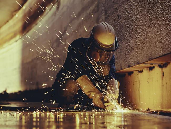 Male worker metal cutting spark on tank bottom steel plate with flash of cutting light close up wear protective gloves and mask in side confined space.