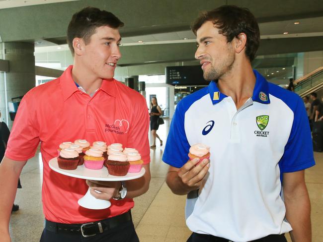 Ashton Agar is given a pink cup cake by fellow Australian player Matt Renshaw to mark the Pink test as he arrives at Sydney Airport on Saturday.