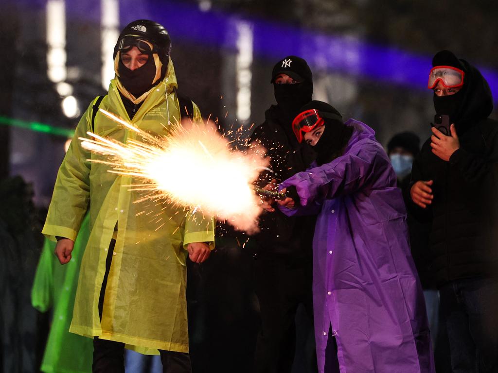 Two protesters dressed in raincoats and ski masks shoot fireworks towards police. Picture: Giorgi ARJEVANIDZE / AFP