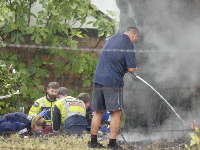 A man uses a garden hose to douse the flames as paramedics perform CPR on the woman in the background. Picture: Careflight