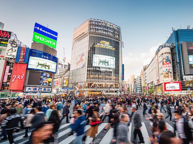 Panorama Shot of People crossing the crowded famous Shibuya Crossing in Downtown Tokyo, illuminated Shibuya Buildings with billboards in the background. Twilight light, close to sunset. Shibuya Crossing, Shibuya Ward, Tokyo, Japan, Asia.