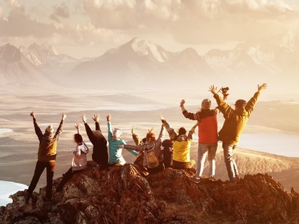 Big group of people having fun in success pose with raised arms on mountain top against sunset lakes and mountains. Travel, adventure or expedition conceptEscape 12 May 2024Doc HolidayPhoto - istock