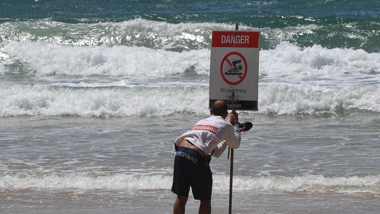 A lifeguard places a ‘no swimming’ sign on a Gold Coast beach on Wednesday. Picture: Dave Hunt