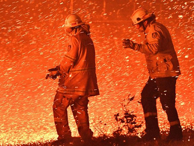 Firefighters struggling against the strong wind in an effort to secure nearby houses from bushfires near the town of Nowra in NSW. Picture: AFP