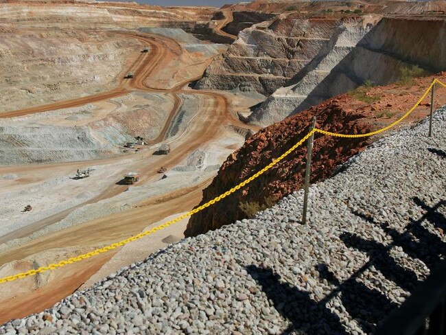 Visitors cast shadows as they look out over part of the main pit of Newcrest Mining Ltd.'s Telfer Mine in the Pilbara region of Western Australia Thursday, July 28, 2005. The mine, which was officially opened today, will be Australia's largest gold and copper producer. Photographer: Will Burgess/Bloomberg News