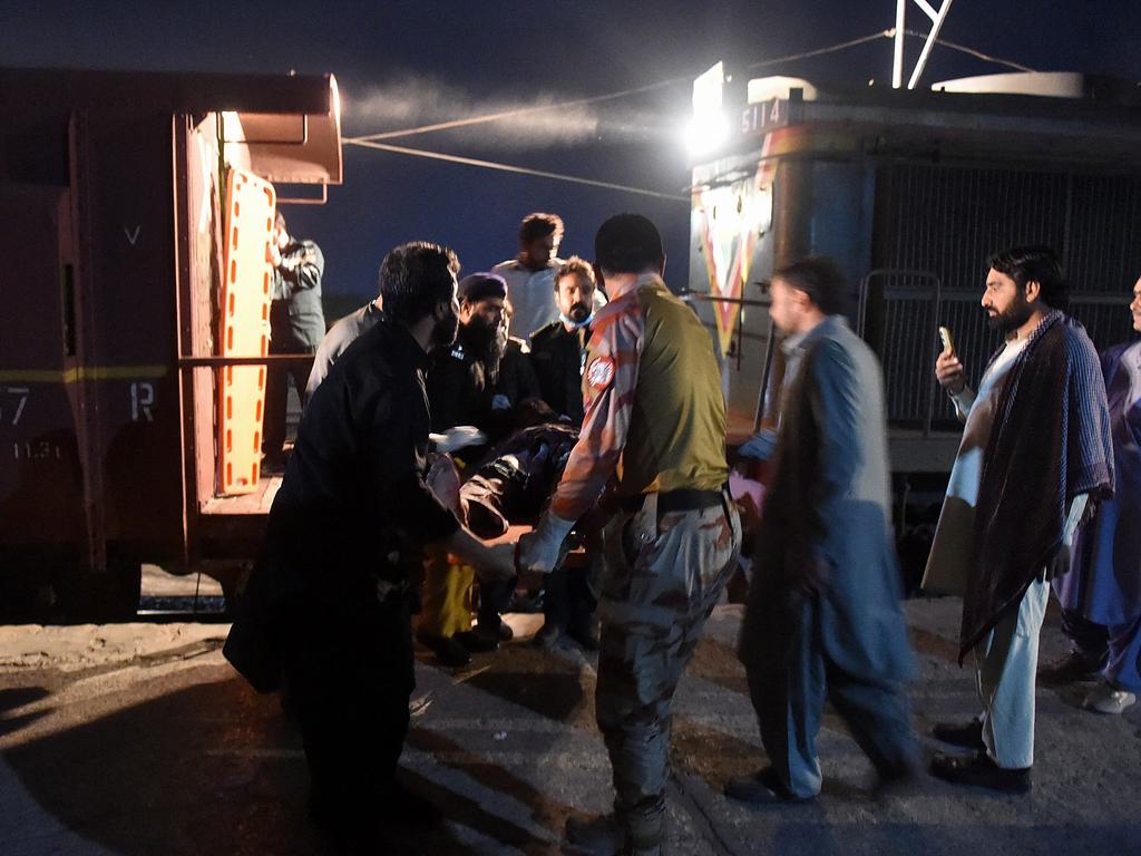 Bystanders help to evacuate an injured passenger on a stretcher at the Mach railway station. Picture: AFP