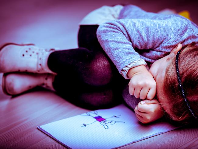 pedophile generic Upset little girl curled up on the bed next to her drawing rubbing her eyes with her fists as though crying, side vignette