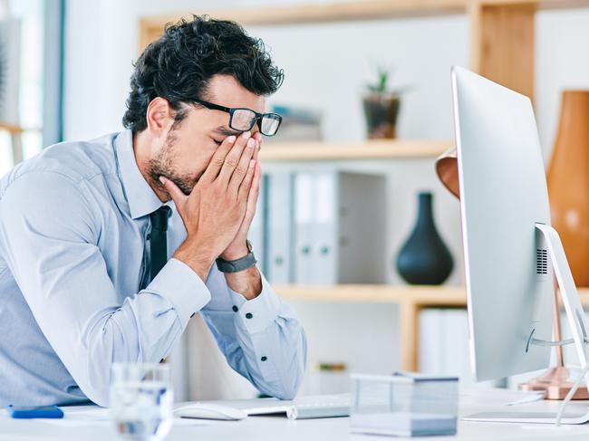 Shot of a young businessman looking stressed out while working on a computer in an office. High functioning anxiety