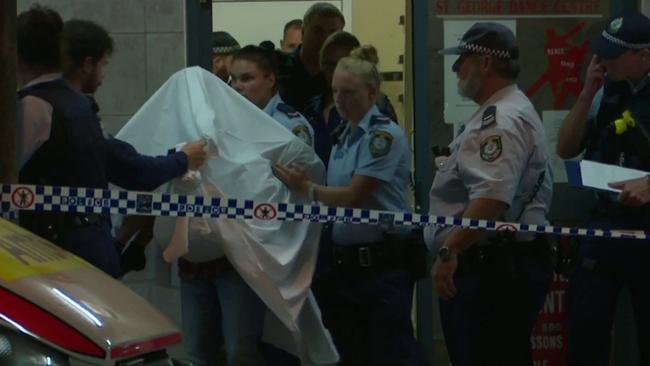 A police officer cradles the girl’s head as she is carried out of the dance studio under a sheet to protect her identity. Picture: TVN