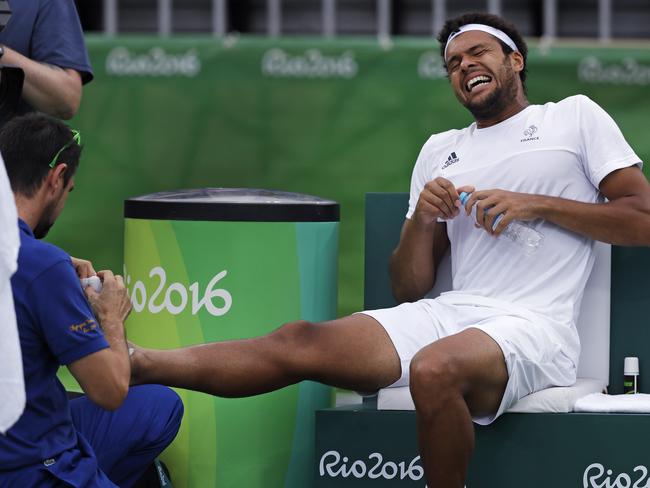 Jo-Wilfried Tsonga, of France, winces in pain as a trainer attends to his injured right foot during a match against Gilles Muller