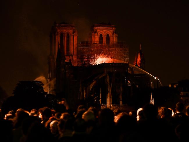 Bystanders look on as flames and smoke billow from the roof at Notre-Dame Cathedral in Paris on April 15, 2019. - A major fire broke out at the landmark Notre-Dame Cathedral in central Paris sending flames and huge clouds of grey smoke billowing into the sky, the fire service said. The flames and smoke plumed from the spire and roof of the gothic cathedral, visited by millions of people a year, where renovations are currently underway. (Photo by FRANCOIS GUILLOT / AFP)