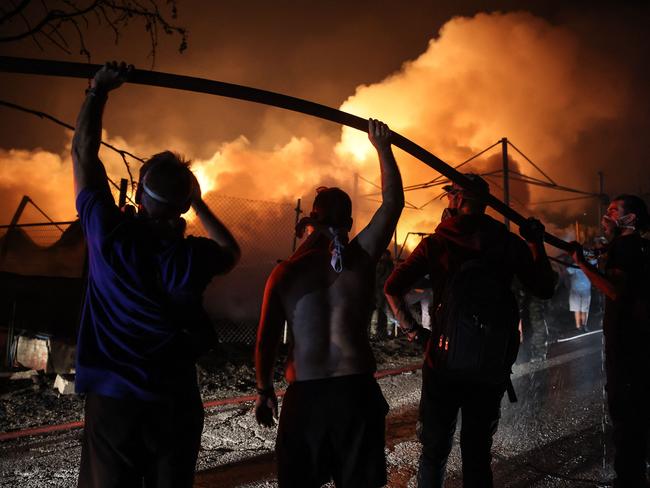 Volunteers hold a water hose in order to help firefighters extinguish a fire in a wood factory in Vrilissia, on the outskirts of Athens. (Photo by Aris Oikonomou / AFP)