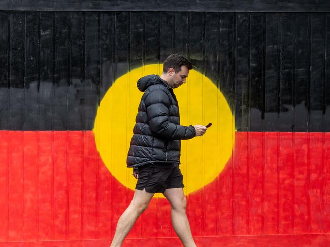 VOICEREF23. A Pedestrian walks past a gate painted in the Aboriginal flag on the day of the referendum in South Yarra, VIC. Melbourne. Picture: Jake Nowakowski