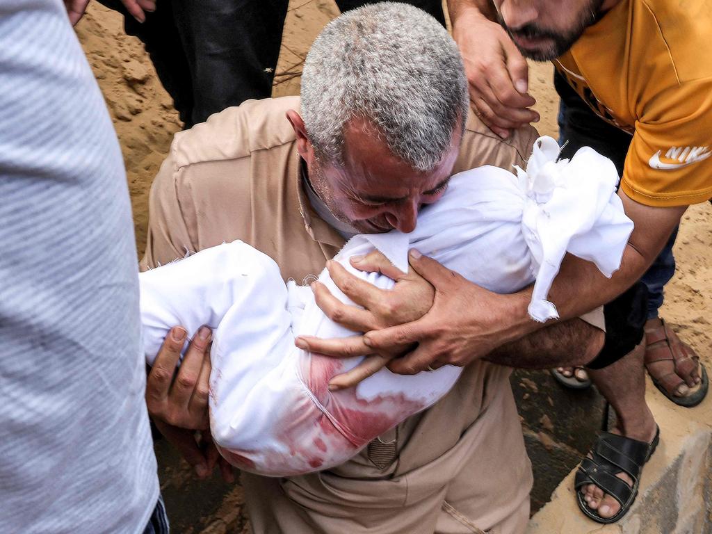 A man reacts as he holds the wrapped body of a child about to be buried at a cemetery in Khan Yunis in the southern Gaza Strip. Picture: AFP