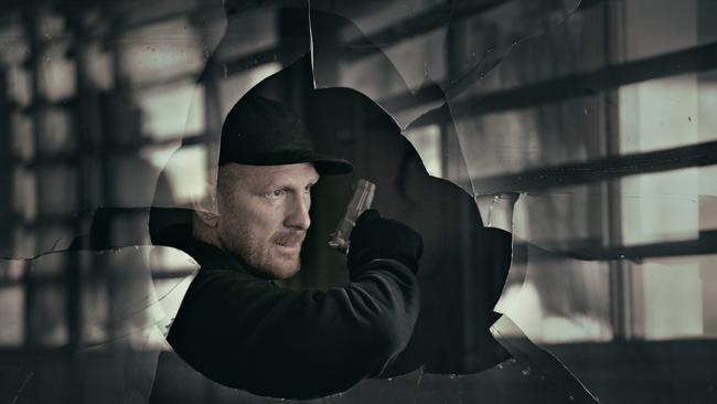 Man wearing a cap holding a gun through a broken window in a dark abandoned warehouse. Istock