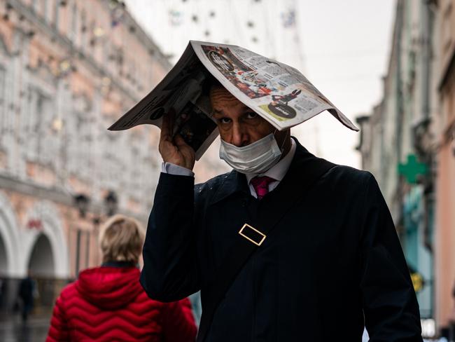 A man wearing a face mask to protect against the COVID-19 disease protects himself from the rain with a newspaper as he walks in central Moscow. Picture: AFP