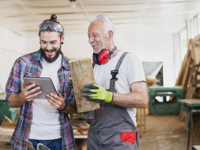 Senior and young carpenter working at workshop using digital tablet