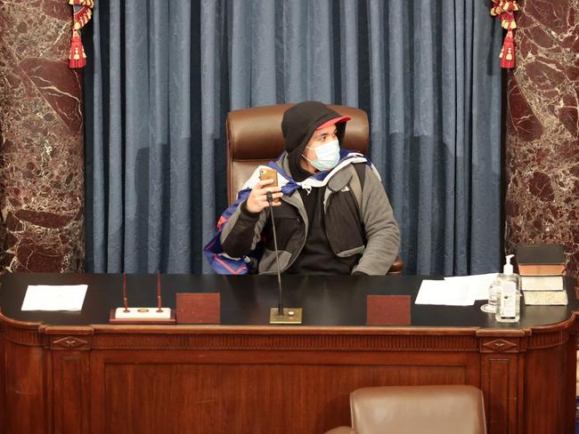 TOPSHOT - WASHINGTON, DC - JANUARY 06: A protester sits in the Senate Chamber on January 06, 2021 in Washington, DC. Congress held a joint session today to ratify President-elect Joe Biden's 306-232 Electoral College win over President Donald Trump. Pro-Trump protesters have entered the U.S. Capitol building after mass demonstrations in the nation's capital.   Win McNamee/Getty Images/AFP (Photo by WIN MCNAMEE / GETTY IMAGES NORTH AMERICA / AFP)