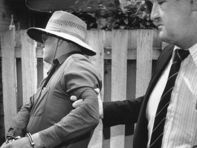 The officer in charge of the Colin Winchester murder investigation, Ric Ninness (right), grips the arm of the handcuffed David Eastman on the day Mr Eastman was charged over the 1989 murder of the top cop. Mr Eastman was acquitted at his 2018 retrial.