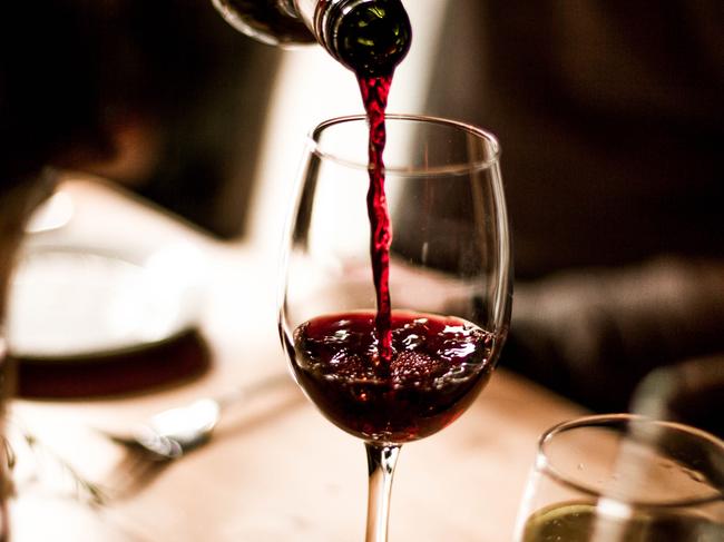 Red wine being poured into a stem glass at the table.