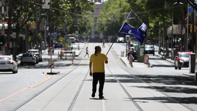 A man marches on Bourke St with a torn Australian flag as part of the protests. Picture: Jake Nowakowski