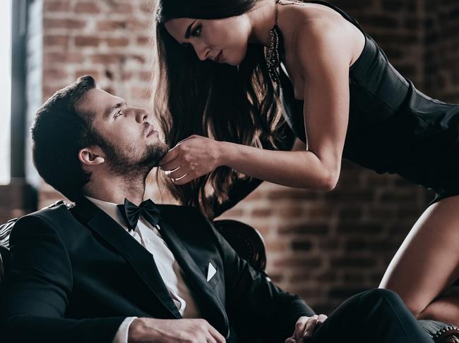 Beautiful young woman in cocktail dress leaning to her boyfriend sitting in chair while looking at each other in loft interior