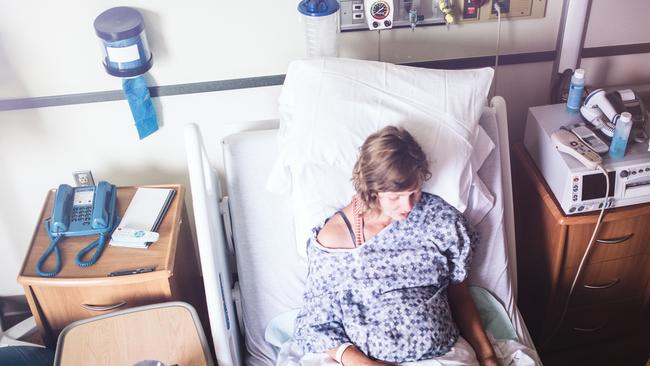 A smiling, happy woman in labor prepares to give birth in a clean white hospital setting.  A depiction of a positive pregnancy and delivery. Horizontal with copy space.