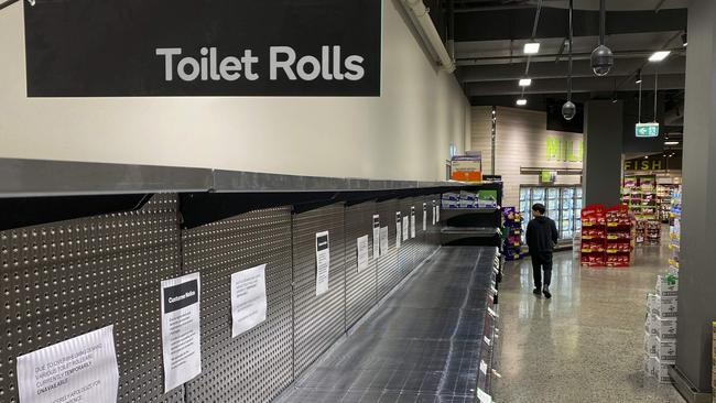 A shopper passes empty shelves usually stocked with toilet paper in a supermarket in Melbourne on March 5, 2020. - COVID-19 coronavirus fears have triggered runs on several products, including hand sanitisers and face masks, with images of shoppers stacking trolleys with toilet rolls spreading on social media. (Photo by William WEST / AFP)