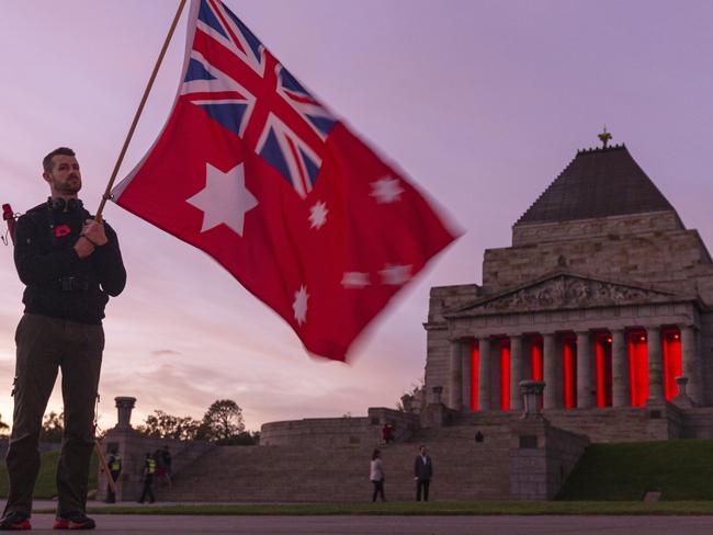 People holding the Australian Red Ensign pay their respects during the Anzac Day Dawn Service at the Shrine of Remembrance in Melbourne, Saturday, April 25, 2020. Anzac Day is a national day of remembrance to commemorate the service and sacrifice of Australian and New Zealand service men and women. Due to COVID-19 restrictions marches and commemorative services have been banned for the first time in more than a century. (AAP Image/Daniel Pockett) NO ARCHIVING