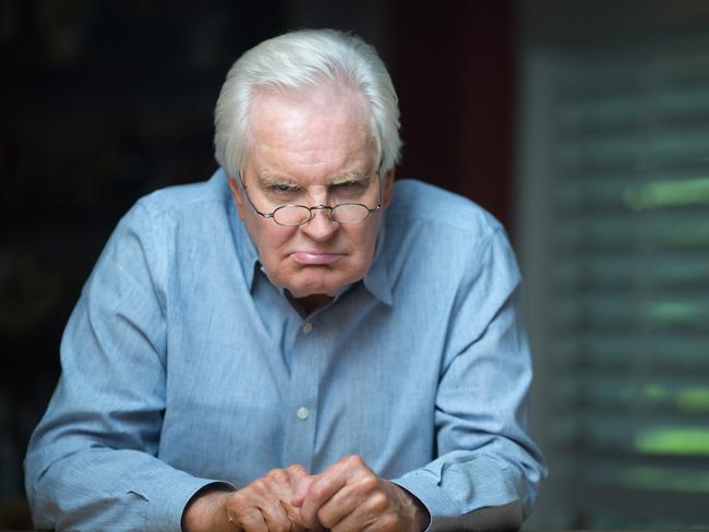 Grumpy old man staring at camera while sitting by the kitchen counter