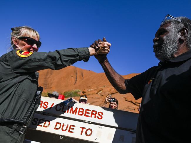 Uluru-Kata Tjuta Ranger Lynda Wright (left) and Chair of the Uluru-Kata Tjuta Council Sidney James shake hands after installing the new sign for the permanent closure of the climb at Uluru, also known as Ayers Rock at Uluru-Kata Tjuta National Park in the Northern Territory, Friday, October 25, 2019. Today is the last day people will be able to climb Uluru. (AAP Image/Lukas Coch) NO ARCHIVING